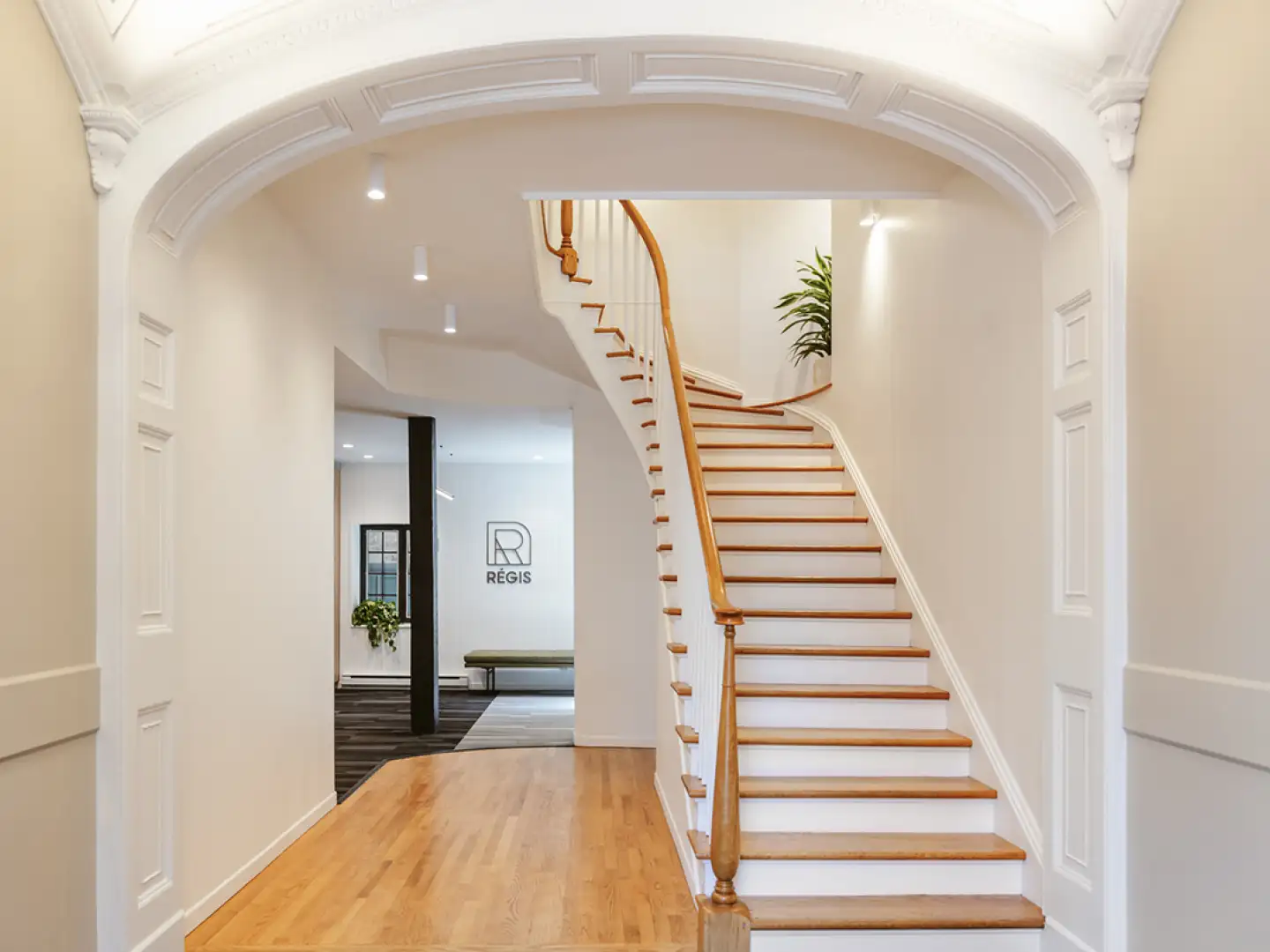 Entrée du bâtiment donnant sur un escalier en bois naturel, offrant une transition chaleureuse et élégante vers l’intérieur.